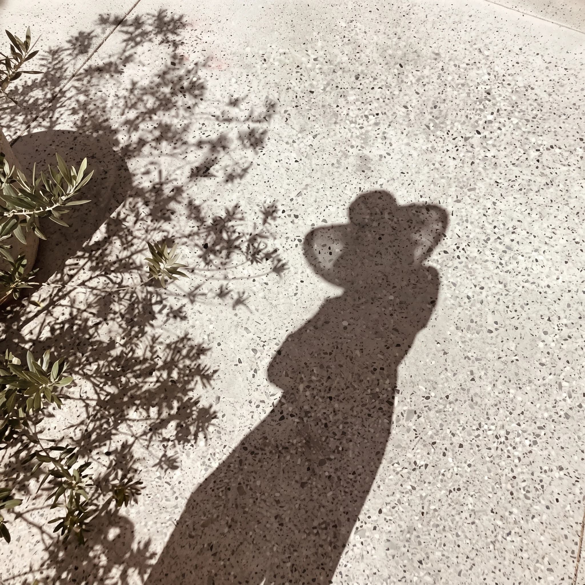Schatten einer Person mit Hut auf warmem Kies, ein ruhiger Moment im Sonnenlicht
